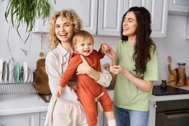 charming joyful lgbt couple playing with their pretty little daughter on kitchen, family concept clipart