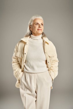 beautiful and grey haired middle aged woman in elegant attire posing on grey background clipart