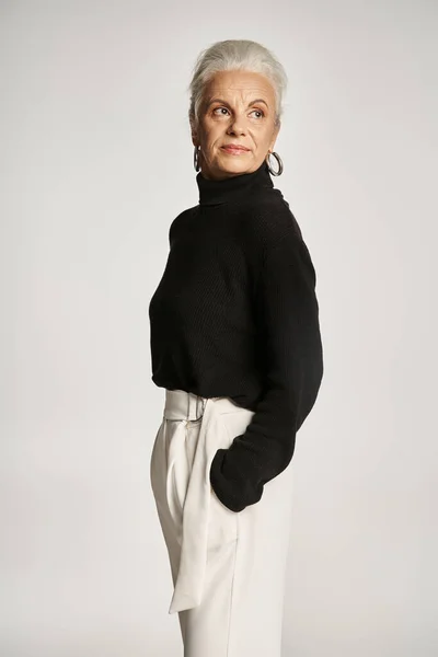 stock image happy middle aged business woman in elegant attire posing with hands in pockets on grey backdrop