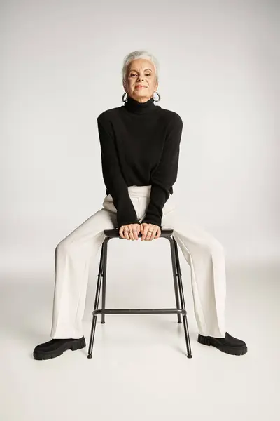 stock image elegant middle aged business woman in smart casual attire and hoop earrings sitting on chair on grey