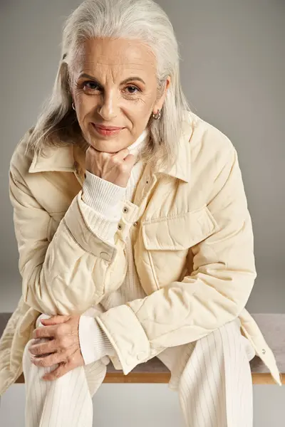 beautiful and grey haired middle aged woman in elegant attire posing on grey background