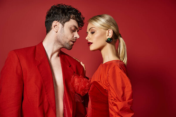 fashionable couple in vibrant attire standing together on red background, man and woman in red