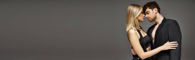 Gri arka planda birbirini kucaklayan çift afişi, siyah elbiseli kadını baştan çıkaran adam.