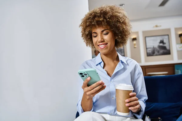 ハッピーカーリー アフリカ系アメリカ人女性コーヒーとホテルのロビーでスマートフォンを使用 — ストック写真
