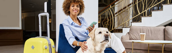 happy african american woman with smartphone sitting near labrador in pet-friendly hotel, banner