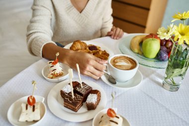 cropped view of african american woman enjoying cappuccino and pastries with room service in a hotel clipart