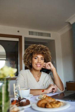 gülümseyen Afrikalı Amerikalı kadın kahvaltıya yakın laptop kullanıyor, oda servisi ve kolaylık