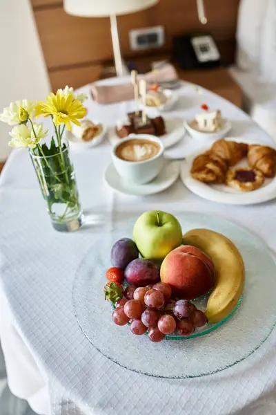 Hotel room service with fresh cappuccino and a variety of breakfast food, flowers and fruits
