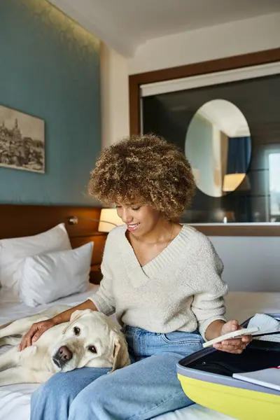 stock image Happy african american woman sitting with labrador near open luggage and checking her smartphone