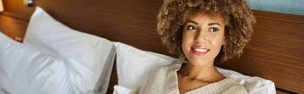 Drömmande Och Glad Afroamerikansk Kvinna Koppla Hotellsäng Och Titta Bort — Stockfoto