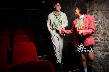 Şık giyinmiş, el ele tutuşan ve birbirlerine gülümseyen neşeli, çekici ve çeşitli çiftler.