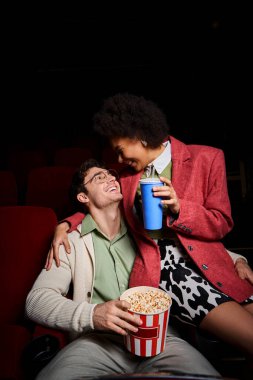 Yakışıklı erkek arkadaşının kucağında oturan ve randevuda ona gülümseyen neşeli Afrikalı Amerikalı kadın.