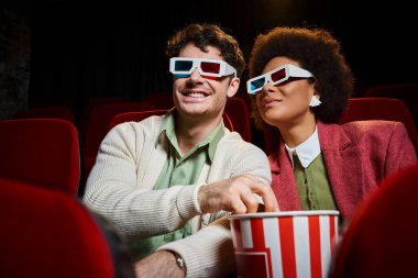 Üç boyutlu gözlüklü neşeli genç çift film izliyor ve randevularında patlamış mısır yiyorlar.
