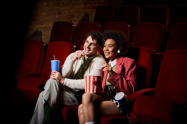 happy young multicultural couple in stylish outfits watching movie on date at cinema, Valentines day