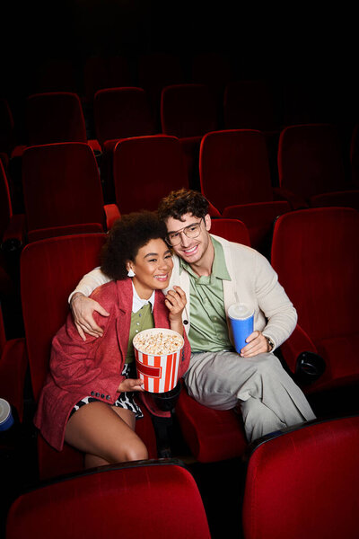 young happy multiethnic couple in casual attires sitting together and enjoying movie on date