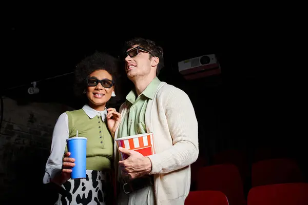 stock image jolly multiethnic couple in 3d glasses holding soft drink and popcorn while on their date at cinema