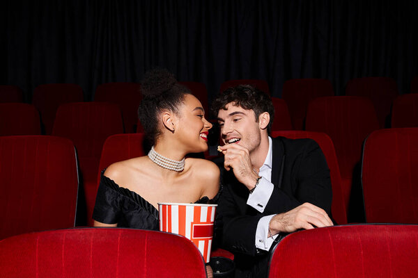good looking man sharing popcorn with his young african american girlfriend on date at cinema