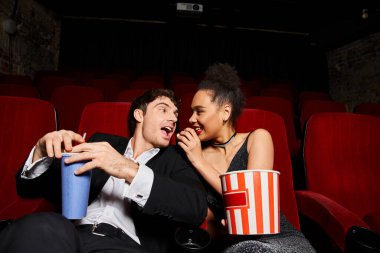 Kırmızı rujlu mutlu Afro-Amerikalı kadın yakışıklı erkek arkadaşıyla patlamış mısır paylaşıyor.