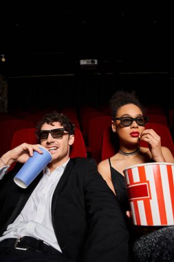 Siyah takım elbiseli yakışıklı adam gülümsüyor ve güzel Afro-Amerikan kadınının yanında oturuyor.