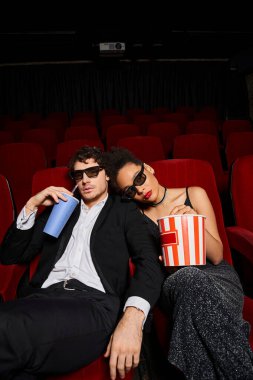 Üç boyutlu gözlüklü çekici çift sevgililer gününde patlamış mısır ve soda ile film izliyorlar.