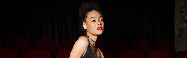 stock image beautiful young african american woman in black dress posing at cinema and looking away, banner