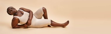 banner of happy plus size african american young woman reclining against beige backdrop clipart