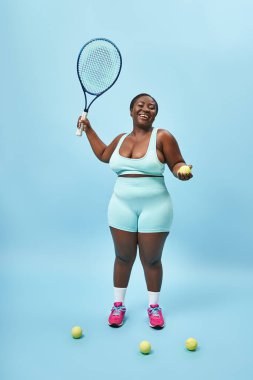 excited plus size dark skinned sportswoman holding tennis racket and ball on blue backdrop, player clipart