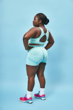 plus size african american woman in stylish active wear looking back and posing with hands on hips clipart