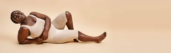 stock image banner of happy plus size african american young woman reclining against beige backdrop