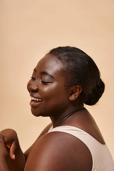 plus size african american model  laughing and posing against beige backdrop, body positive