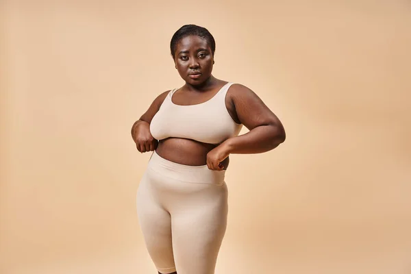 plus size woman in underwear posing on beige backdrop, body positive and female empowerment