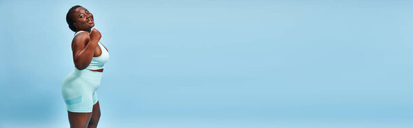 happy plus size woman in active wear flexing her muscles on blue background, horizontal banner