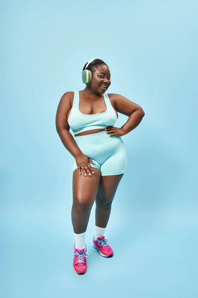 ヘッドフォンでリスニングミュージックを着用するアクティブなアフリカ系アメリカ人女性 ブルーバックドロップ — ストック写真