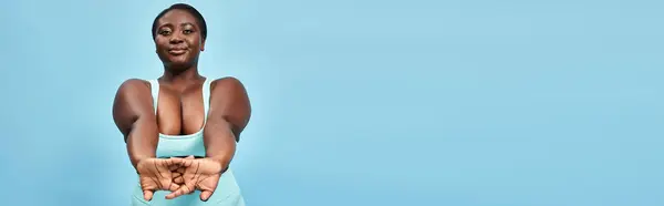 幸せなプラスサイズ アフリカ系アメリカ人女性 アクティブウェア ブルーバックドロップ バナーで喜んで伸びる — ストック写真