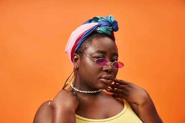 stock image Fashionable plus size and young african american woman in headscarf and trendy sunglasses on orange