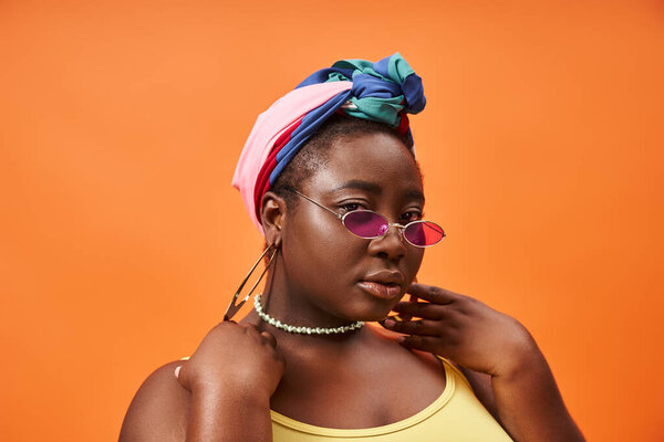 Модный plus size и молодая африканская женщина в платке и трехцветных солнцезащитных очках оранжевого цвета