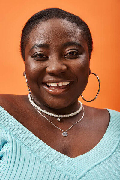 portrait of body positive young african american woman in blue long sleeve on orange background