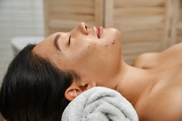 asian woman with closed eyes lying with closed eyes in wellness center, spa and facial treatment