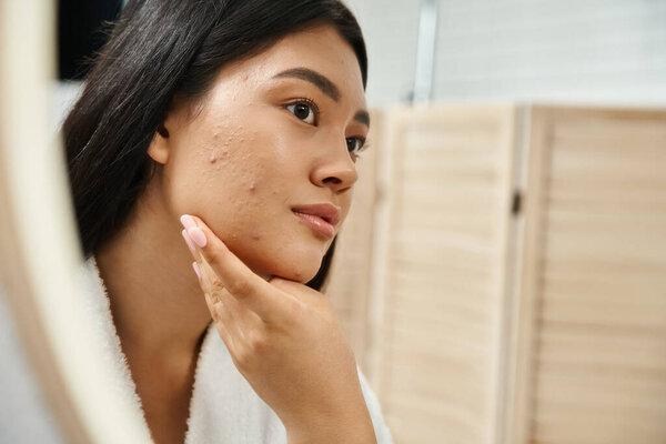 young asian woman with brunette hair and acne prone skin looking at mirror in bathroom, banner