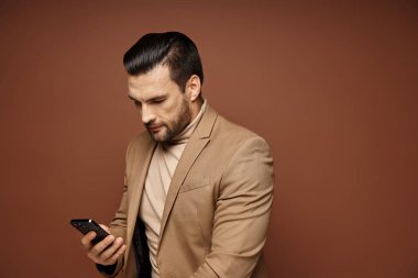 Zarif giyimli yakışıklı iş adamı bej arka planda akıllı telefonunu kontrol ediyor.