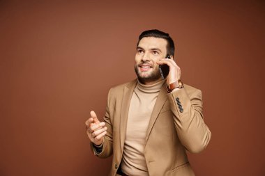 Ceketli şık ve yakışıklı bir adam gülümsüyor ve akıllı telefondan bej bir fon arıyor.