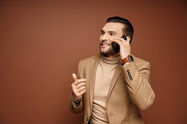 şık ceketli yakışıklı adam gülümsüyor ve akıllı telefondan, bej arka planda telefon görüşmesi yapıyor.