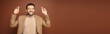 banner of attractive man in elegant attire smiling with his fingers crossed on beige background clipart