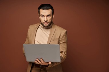 Odaklanmış ve yakışıklı profesyonel bilgisayarını tutarken bej arka plan üzerinde çalışıyor.