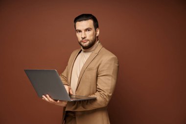 Odaklanmış ve yakışıklı iş adamı bej arka plan üzerinde çalışırken dizüstü bilgisayarını tutuyor.