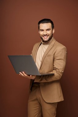 Mutlu ve yakışıklı iş adamı bej arka plan üzerinde çalışırken dizüstü bilgisayarını tutuyor.