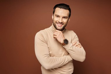 Boğazlı kazak giymiş mutlu adam bej arka planda çenesine dokunuyor, erkek model.