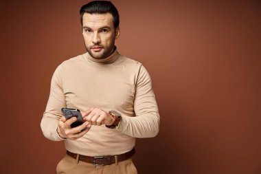 Balıkçı yaka kazaklı yakışıklı adam bej arka planda akıllı telefonunu kullanıyor, sosyal medya...