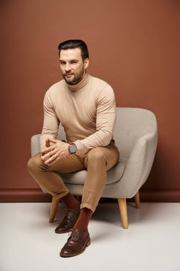 Tüylü yakışıklı ve kurnaz adam bej arka planda rahat koltukta oturuyor.