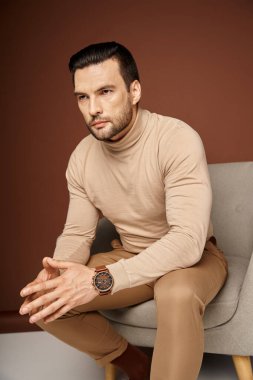 Balıkçı yakalı ve ciddi bir adam bej arka planda rahat koltukta oturuyor.